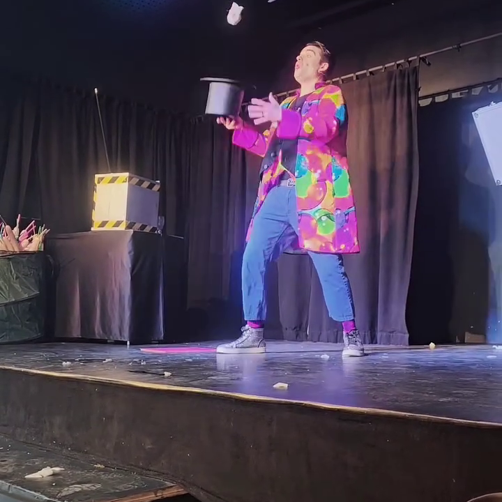 Kinderzauberer Maik - Zaubervorstellung Ein Kinderzauberer in buntem Kostüm führt einen Trick auf der Bühne vor.